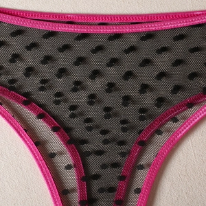 Detail of black polka dot mesh fabric with vibrant pink elastic trim on women's lingerie