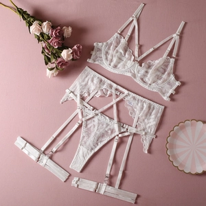Detailed flat lay of white lace lingerie set with bra, garter belt, and thong on pink background
