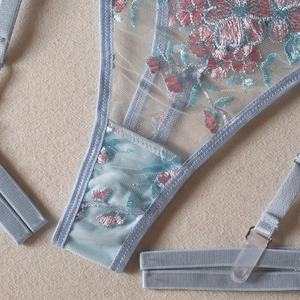 Close-up of light blue floral embroidery on sheer mesh lingerie with adjustable straps
