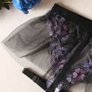 Détail de lingerie en maille noire transparente avec broderie florale violette et bretelles réglables
