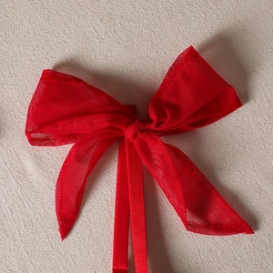Close-up of a large red mesh bow with ribbons on a textured beige fabric surface