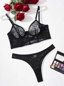 Flat lay of black floral lace lingerie set with mesh bra and thong on white background