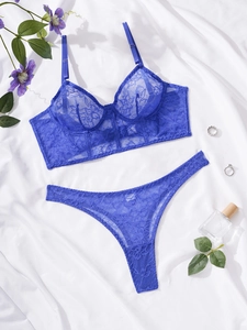 Flat lay of royal blue lace bra and thong set with floral patterns on white silk fabric