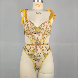 Detail of yellow mesh bodysuit featuring colorful floral embroidery and satin bow straps