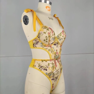 Detail of floral embroidery on yellow sheer mesh bodysuit with vibrant lace shoulder ties