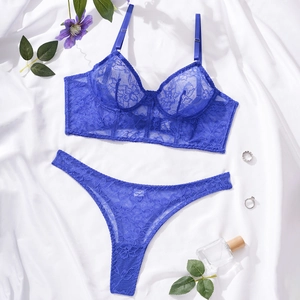 Flat lay of navy blue lace bralette and thong set on white silk background with flowers