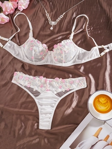 Détail de fleurs roses et jaunes brodées sur de la lingerie en dentelle blanche et satin