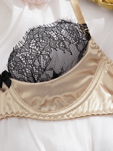 Detail eines Satin-BHs mit schwarzer Wimpernspitze und Schleife auf champagnerfarbenem Stoff