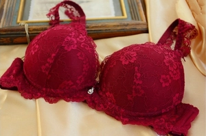 Detail of wine red lace bra with padded cups and silver heart pendant on satin fabric