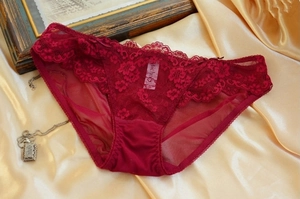 Detailed close-up of dark red floral lace panties with a bow on gold satin fabric