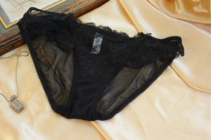 Detail of black lace mesh panties with satin bows on luxurious gold satin background