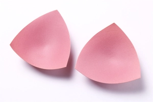 Macro view of pink triangular sponge bra pads with smooth fabric surface and neat edges