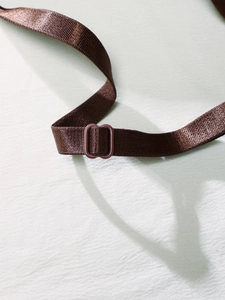 Detailed macro view of dark brown adjustable strap and slide buckle for seamless bodysuit