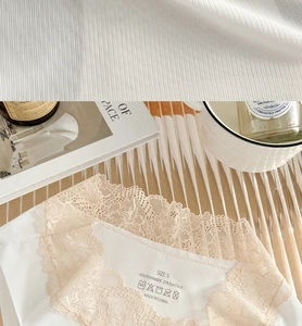 Dettaglio del tessuto a coste bianco con pizzo floreale beige ed etichetta taglia S