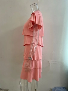 Detail of coral pink tiered dress showing multilayered ruffled skirt and soft fabric texture