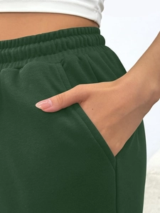 Detail view of high-waist drawstring waistband and side pockets on dark green joggers