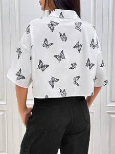 Vista trasera de una camisa corta blanca con estampados de mariposas negras y hombros caídos