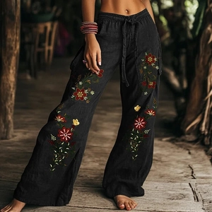 Detail van een zwarte bohemien broek met wijde pijpen, bloemenborduursels en trekkoord