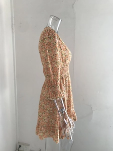 Detailed view of elastic smocked waist and orange floral print on a long sleeve dress