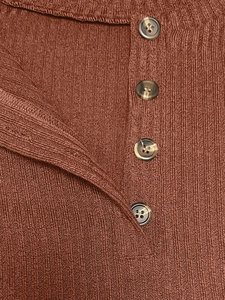 Detail of rust red ribbed knit fabric featuring amber marble-textured buttons on the front