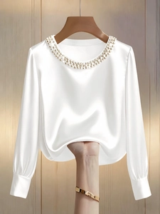 Detail of elegant white satin blouse with pearl-embellished crew neck and smooth texture