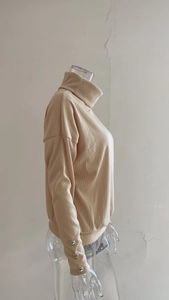 Detail of ribbed knit sweater sleeve featuring three decorative silver metal buttons