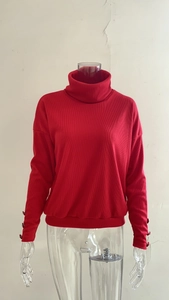 Detail of red turtleneck sweater featuring vertical ribbing and decorative cuff buttons