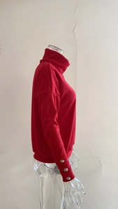 Detail of red ribbed knit sweater featuring silver decorative buttons on sleeve cuffs