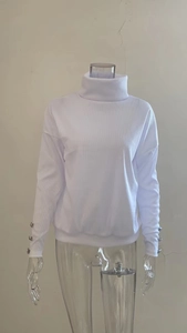 Close-up of white ribbed knit turtleneck sweater featuring silver buttons on sleeve cuffs