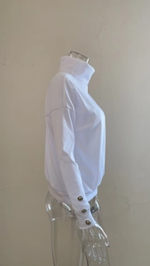 Detail of white ribbed knit sweater featuring silver buttons on the cuffs and high neck collar