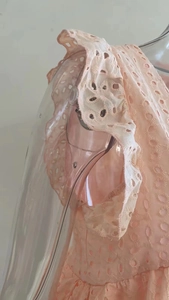 Dettaglio dell'abito rosa chiaro con maniche a balze e ricami in pizzo floreale