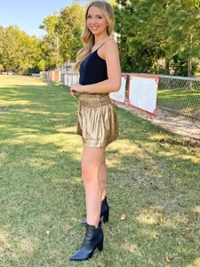 Outdoor shot of shimmering gold metallic shorts paired with a black camisole top