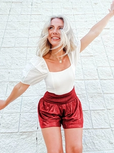 Detail of red metallic high-waisted shorts with pleated texture and elastic waistband