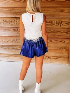 Back view of high-waist metallic blue shorts and white sleeveless top with feather trim