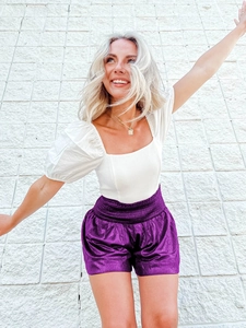 Detail of high waist purple shiny shorts with elastic waistband and puff sleeve crop top