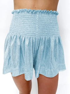 Detail of light blue high-waisted smocked shorts with ruffled hem and textured fabric