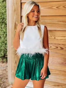 Detail of white sleeveless top with feather trim and green metallic pleated shorts