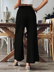 Detail of high-waisted black wide-leg trousers featuring pleated texture and elastic waist