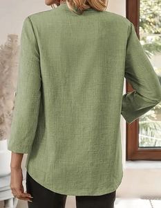 Detail of green long-sleeve cotton linen top showing natural fabric texture and curved hem