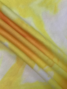 Close-up detail of soft knitted fabric with bright yellow and orange tie-dye pattern