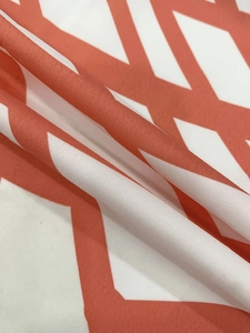 Close-up of coral orange and white geometric pattern on soft polyester blend fabric