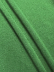 Close-up of bright green knit fabric texture and soft drape of elegant women's trousers
