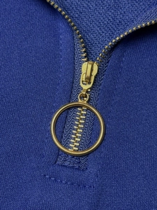 Detailed macro shot of a gold circular zipper pull on dark blue knitted fabric
