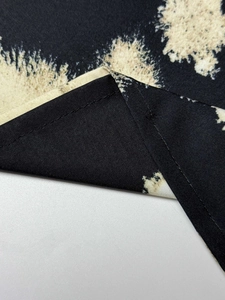 Macro shot of black fabric with beige tie-dye print and precise stitching edges