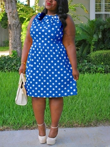 Outdoor shot of sleeveless blue polka dot plus size dress with bow tie neckline detail