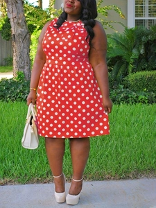 Close-up of a plus size red sleeveless dress with white polka dots in a lawn setting