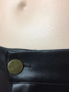 Detailaufnahme der Kunstlederhose mit hoher Taille, Bronzeknopf und Lychee-Struktur
