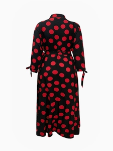 Back view of a long-sleeved black dress with large red polka dots and waist tie detail