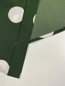 Detail of the dark green fabric with white polka dots showing stitching and texture