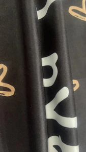 Detail shot of black fabric with white letter prints and brown heart graffiti patterns